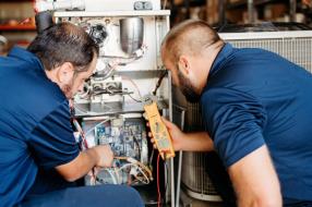 Two Colony technicians testing a furnace with a multimeter in Plano