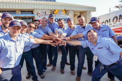 Colony technicians stacking hands in a team huddle outside the office in The Colony