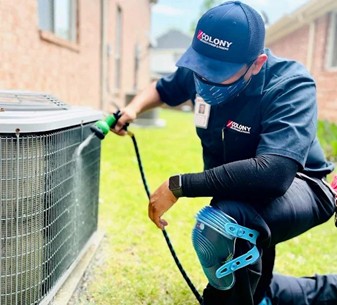 Outdoor AC condenser maintenance and cleaning being done by a Colony technician.