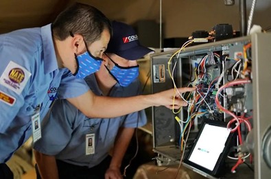 Two uniformed Colony Air Conditioning & Heating technicians inspect the wiring of an air handler as part of a Carrollton AC repair visit.